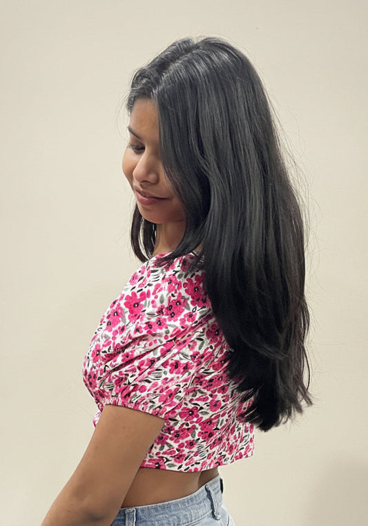 Woman wearing a pink floral crop top and blue jeans against a plain background