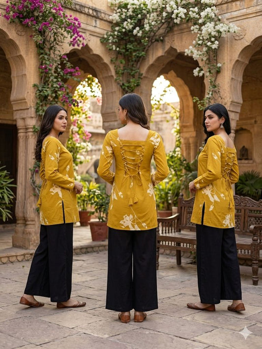 Woman in a yellow top and black pants standing in a courtyard with arches and plants.